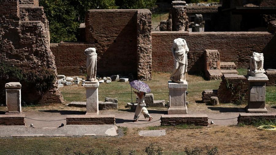 Seorang wanita menggunakan payung untuk berlindung dari terik matahari saat mengunjungi Forum Romawi di tengah suhu yang mendekati 40 derajat Celsius akibat gelombang panas, di Roma, Italia, pada 11 Agustus 2026. (REUTERS/Guglielmo Mangiapane)