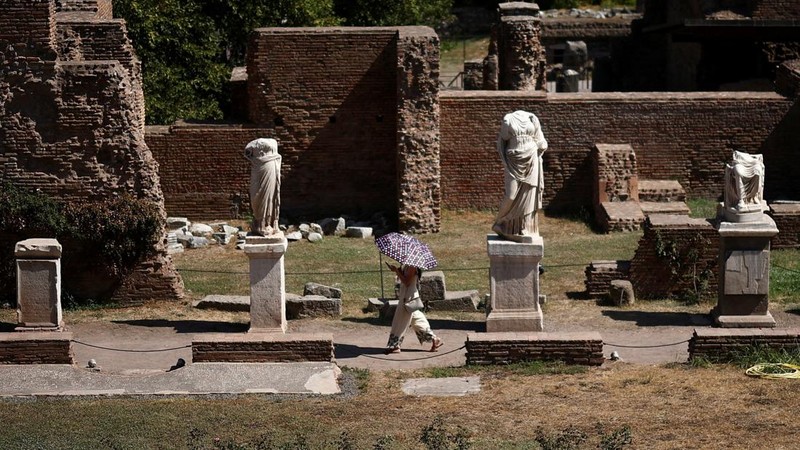 Seorang wanita menggunakan payung untuk berlindung dari terik matahari saat mengunjungi Forum Romawi di tengah suhu yang mendekati 40 derajat Celsius akibat gelombang panas, di Roma, Italia, pada 11 Agustus 2026. (REUTERS/Guglielmo Mangiapane)