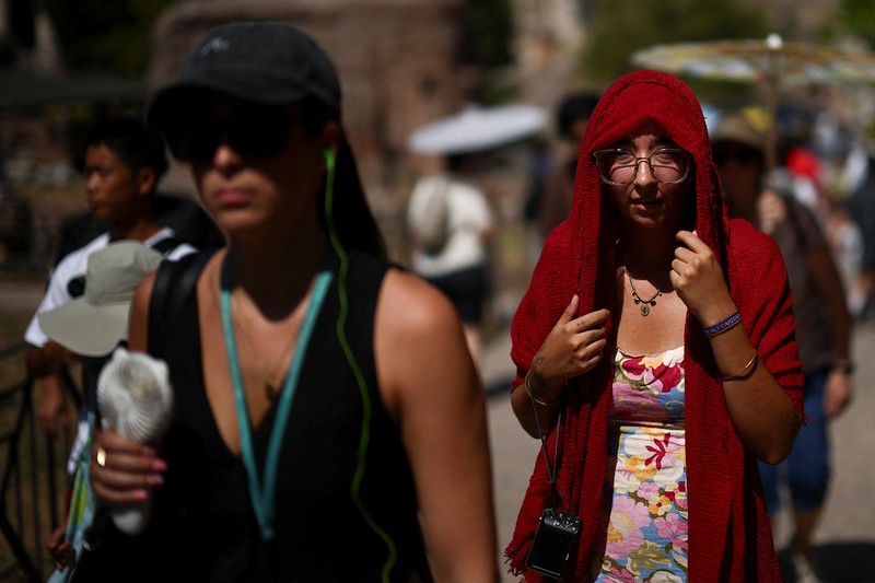 Seorang wanita menggunakan payung untuk berlindung dari terik matahari saat mengunjungi Forum Romawi di tengah suhu yang mendekati 40 derajat Celsius akibat gelombang panas, di Roma, Italia, pada 11 Agustus 2026. (REUTERS/Guglielmo Mangiapane)