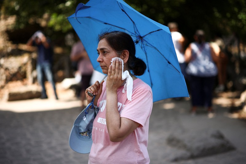 Seorang wanita menggunakan payung untuk berlindung dari terik matahari saat mengunjungi Forum Romawi di tengah suhu yang mendekati 40 derajat Celsius akibat gelombang panas, di Roma, Italia, pada 11 Agustus 2026. (REUTERS/Guglielmo Mangiapane)