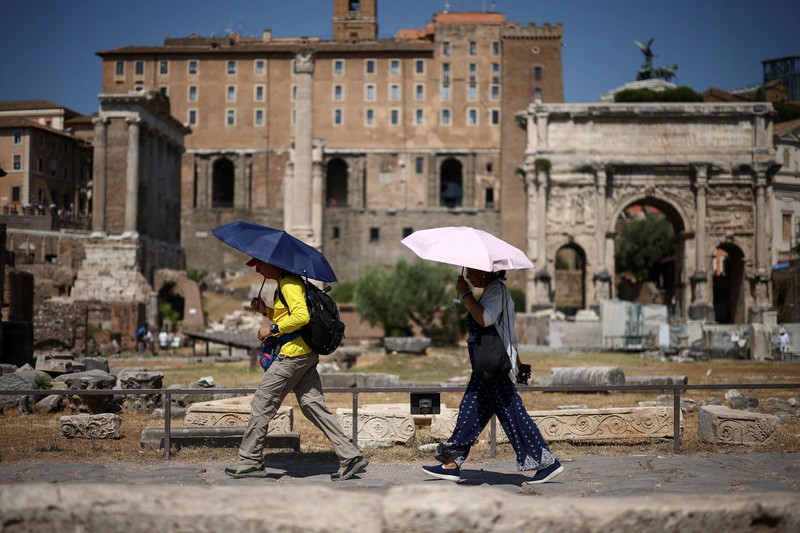 Seorang wanita menggunakan payung untuk berlindung dari terik matahari saat mengunjungi Forum Romawi di tengah suhu yang mendekati 40 derajat Celsius akibat gelombang panas, di Roma, Italia, pada 11 Agustus 2026. (REUTERS/Guglielmo Mangiapane)