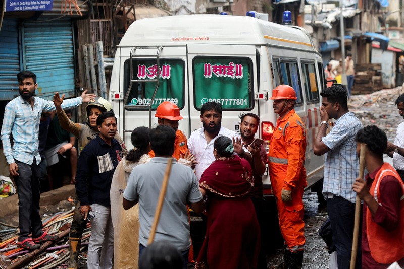 Warga menyaksikan petugas Pasukan Tanggap Bencana Nasional (NDRF) berjalan menuju lokasi tanah longsor setelah sebagian bukit runtuh menimpa rumah-rumah di kawasan permukiman kumuh di Mumbai, India, pada 12 Agustus 2026. (REUTERS/Francis Mascarenhas)