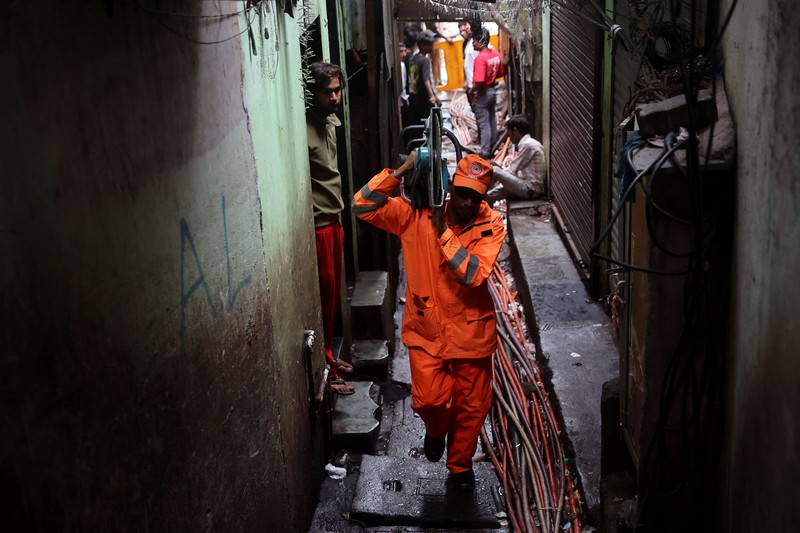 Warga menyaksikan petugas Pasukan Tanggap Bencana Nasional (NDRF) berjalan menuju lokasi tanah longsor setelah sebagian bukit runtuh menimpa rumah-rumah di kawasan permukiman kumuh di Mumbai, India, pada 12 Agustus 2026. (REUTERS/Francis Mascarenhas)