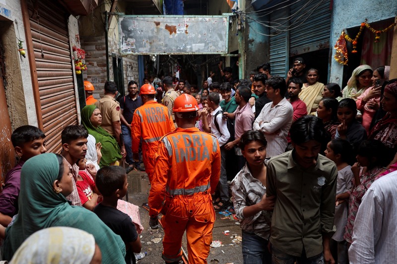 Warga menyaksikan petugas Pasukan Tanggap Bencana Nasional (NDRF) berjalan menuju lokasi tanah longsor setelah sebagian bukit runtuh menimpa rumah-rumah di kawasan permukiman kumuh di Mumbai, India, pada 12 Agustus 2026. (REUTERS/Francis Mascarenhas)