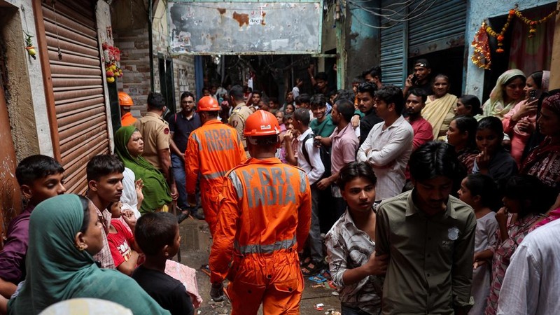 Warga menyaksikan petugas Pasukan Tanggap Bencana Nasional (NDRF) berjalan menuju lokasi tanah longsor setelah sebagian bukit runtuh menimpa rumah-rumah di kawasan permukiman kumuh di Mumbai, India, pada 12 Agustus 2026. (REUTERS/Francis Mascarenhas)