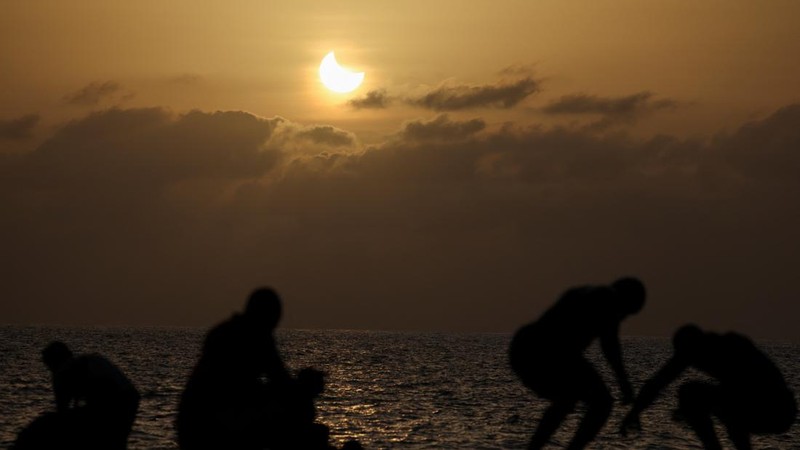 Warga berolahraga di sepanjang pantai saat bulan menutupi sebagian matahari dalam peristiwa gerhana matahari sebagian di Dakar, Senegal, pada 12 Agustus 2026.