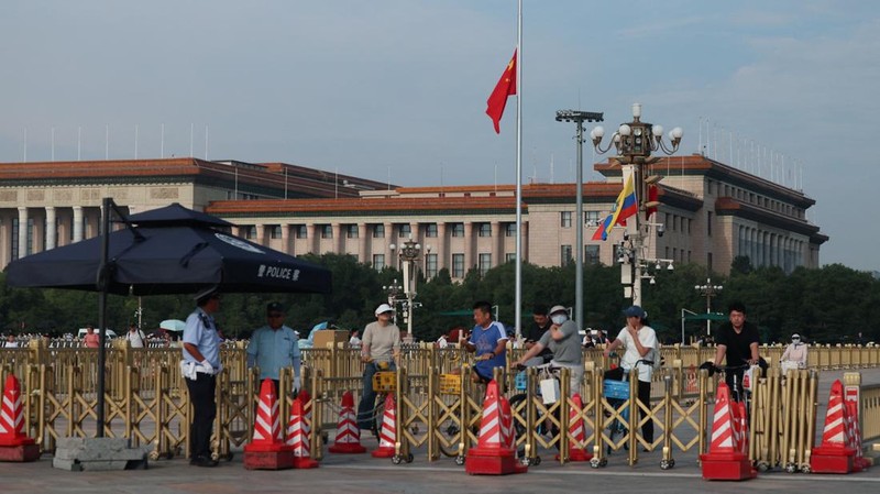 People wait for the traffic light at a police barricade, with the Great Hall of the People in the background, as the Chinese flag at Tiananmen Square flies at half-mast in memory of the late Former Chinese Premier Zhu Rongji, who passed away last Wed