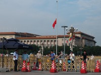 People wait for the traffic light at a police barricade, with the Great Hall of the People in the background, as the Chinese flag at Tiananmen Square flies at half-mast in memory of the late Former Chinese Premier Zhu Rongji, who passed away last Wed