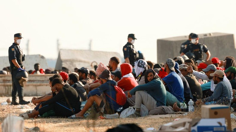 Para migran berkumpul di dekat sebuah kamp darurat di tepi pantai untuk dipindahkan ke tempat penampungan resmi di berbagai lokasi di kota tersebut setelah pihak berwenang membersihkan area itu—menyusul penyeberangan massal dari Maroko—di wilayah kantong Spanyol di Afrika Utara, Ceuta, pada 20 Agustus 2026.