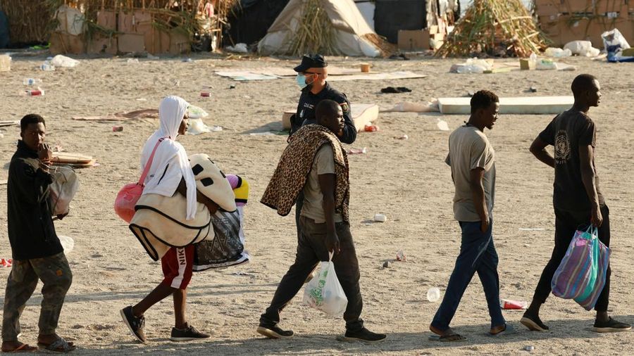 Para migran dikawal dari kamp darurat di pantai menuju tempat penampungan resmi di berbagai lokasi di kota tersebut setelah pihak berwenang membersihkan area itu—menyusul penyeberangan massal dari Maroko—di wilayah kantong Spanyol di Afrika Utara, Ceuta, pada 20 Agustus 2026.