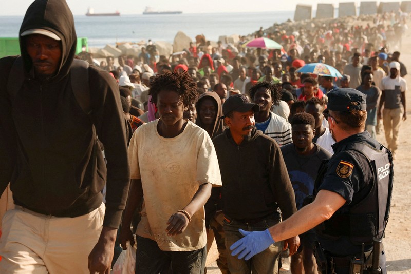 Para migran dikawal dari kamp darurat di pantai menuju tempat penampungan resmi di berbagai lokasi di kota tersebut setelah pihak berwenang membersihkan area itu&mdash;menyusul penyeberangan massal dari Maroko&mdash;di wilayah kantong Spanyol di Afrika Utara, Ceuta, pada 20 Agustus 2026. (REUTERS/Violeta Santos Moura)