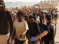 Para migran dikawal dari kamp darurat di pantai menuju tempat penampungan resmi di berbagai lokasi di kota tersebut setelah pihak berwenang membersihkan area itumenyusul penyeberangan massal dari Marokodi wilayah kantong Spanyol di Afrika Utara, Ceut