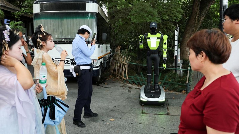 Orang-orang berjalan melewati polisi lalu lintas robot humanoid yang dikembangkan oleh SUPCON saat robot tersebut sedang bertugas di sebuah jalan di Hangzhou, Provinsi Zhejiang, Tiongkok, pada 21 Juli 2026.