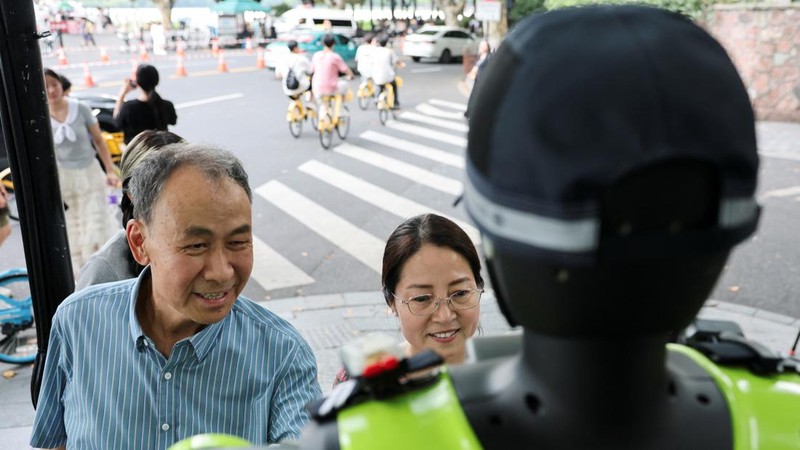 Warga berinteraksi dengan robot polisi lalu lintas berbentuk manusia yang dikembangkan oleh SUPCON saat robot tersebut sedang bertugas di sebuah jalan di Hangzhou, Provinsi Zhejiang, Tiongkok, pada 21 Juli 2026.