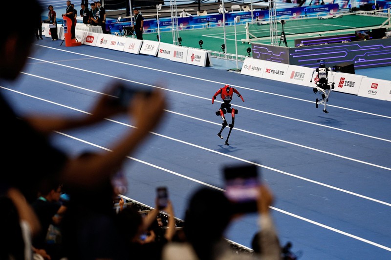 Robot humanoid Honor dan Tiangong bertanding dalam lomba penyisihan kategori kelompok besar jarak 100 meter,etelah upacara pembukaan World Humanoid Robot Games 2026, di National Speed ​​Skating Oval, Beijing, China, Sabtu (22/8/20265). (REUTERS/Tingshu Wang)