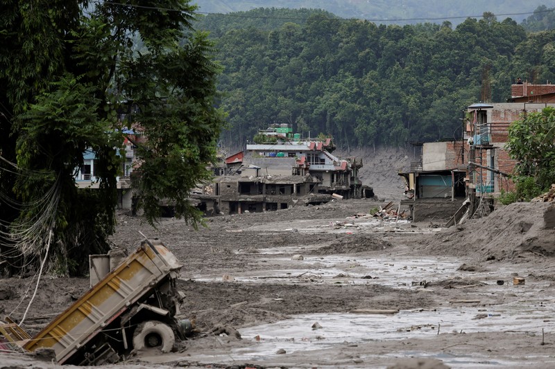 Warga berdiri di dekat rumah-rumah yang tertutup lumpur dan sebuah jalan setelah banjir bandang di Trishuli, Distrik Nuwakot, Nepal, pada 26 Agustus 2026. (REUTERS/Navesh Chitrakar)