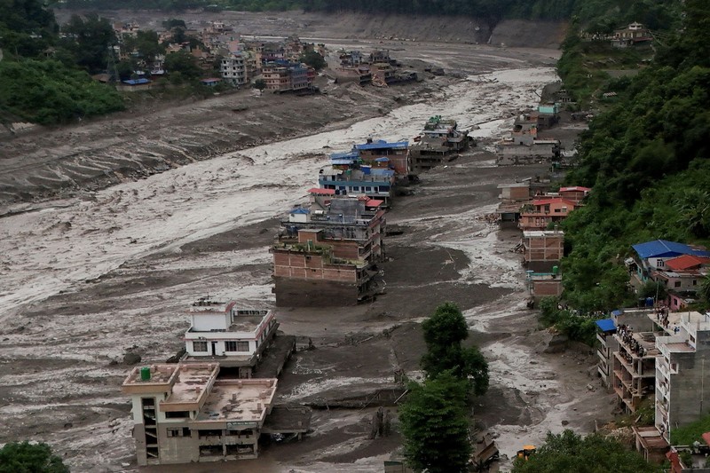 Warga berdiri di dekat rumah-rumah yang tertutup lumpur dan sebuah jalan setelah banjir bandang di Trishuli, Distrik Nuwakot, Nepal, pada 26 Agustus 2026. (REUTERS/Navesh Chitrakar)