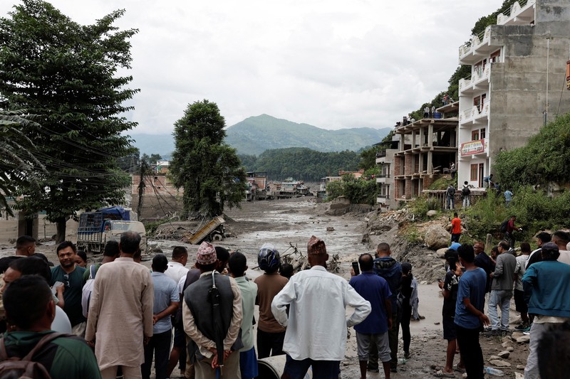 Warga berdiri di dekat rumah-rumah yang tertutup lumpur dan sebuah jalan setelah banjir bandang di Trishuli, Distrik Nuwakot, Nepal, pada 26 Agustus 2026. (REUTERS/Navesh Chitrakar)