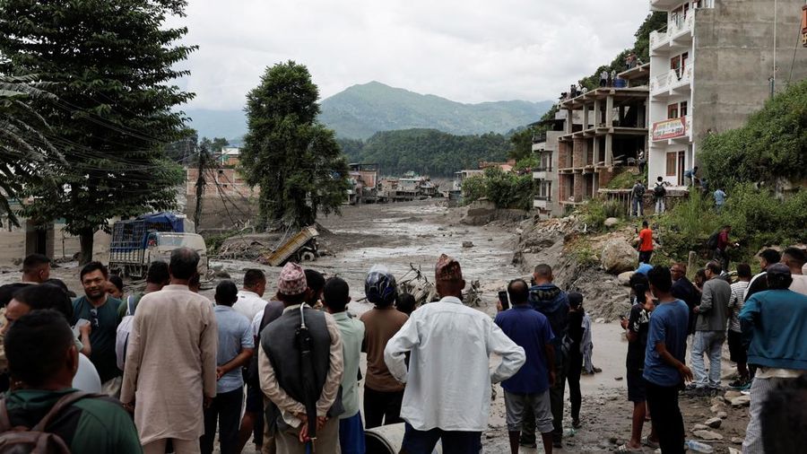 Warga berdiri di dekat rumah-rumah yang tertutup lumpur dan sebuah jalan setelah banjir bandang di Trishuli, Distrik Nuwakot, Nepal, pada 26 Agustus 2026. (REUTERS/Navesh Chitrakar)