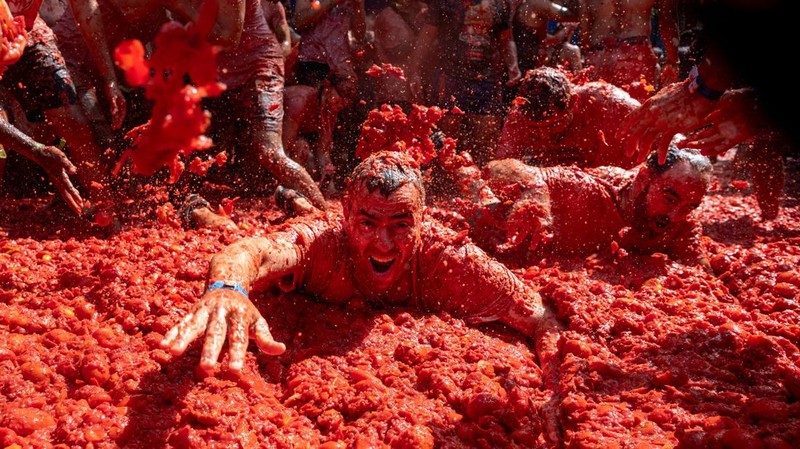 Para peserta bersenang-senang di tengah bubur tomat dalam festival perang makanan tahunan