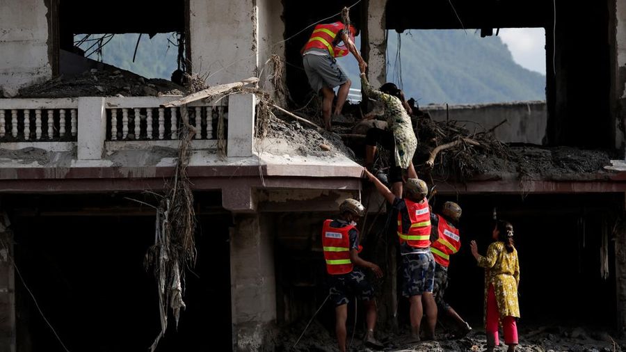 Tim penyelamat membantu seorang wanita masuk ke rumahnya yang rusak untuk menyelamatkan barang-barangnya setelah banjir bandang dan tanah longsor di Trishuli, distrik Nuwakot, Nepal, pada 28 Agustus 2026.