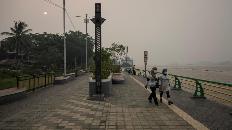 Warga yang mengenakan masker pelindung berjalan di tepi Sungai Kapuas saat kabut asap akibat kebakaran hutan menyelimuti kawasan tersebut di Pontianak, Provinsi Kalimantan Barat, Indonesia, pada 27 Agustus 2026.