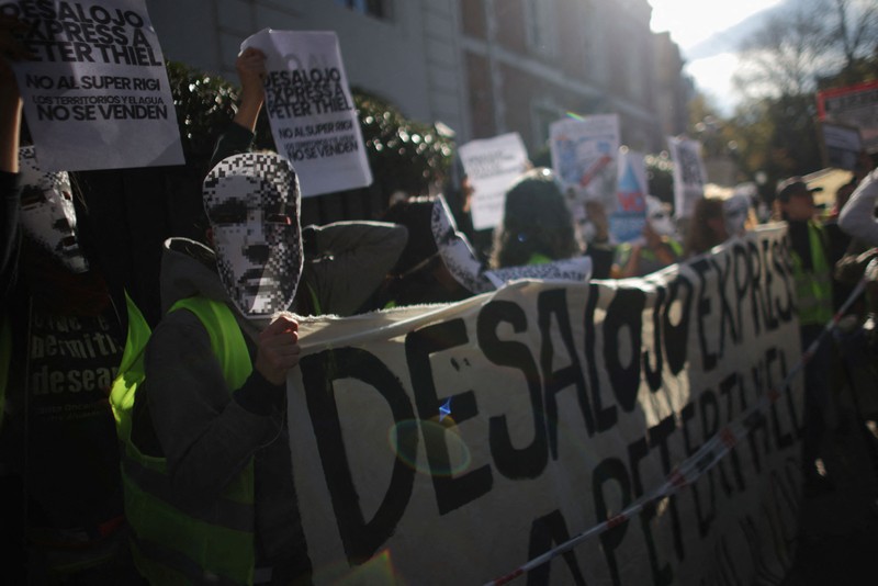 Para pengunjuk rasa membawa plakat dan boneka saat melakukan aksi long march di kediaman Peter Thiel&mdash;salah satu pendiri Palantir dan pemegang saham baru di Vista Energy&mdash;dengan seruan