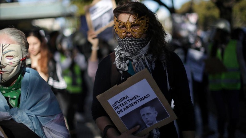Seorang pengunjuk rasa memegang plakat saat melakukan pawai menuju kediaman Peter Thiel—salah satu pendiri Palantir dan pemegang saham baru di Vista Energy—dengan seruan