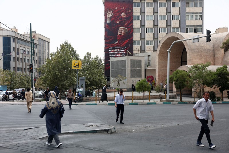 Warga berkendara di dekat papan reklame yang menampilkan Presiden AS Donald Trump pada sebuah gedung di Teheran, Iran, Senin (31/8/2026). (Majid Asgaripour/WANA via REUTERS)