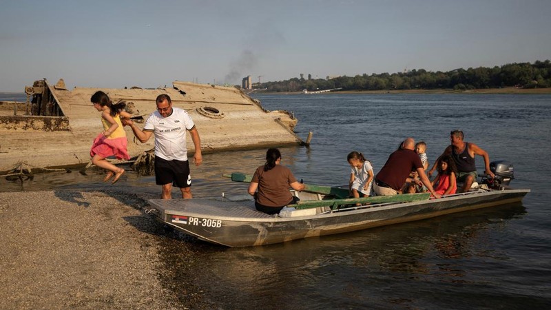 Seorang gadis melompat saat orang-orang turun dari perahu menuju gosong pasir di samping bangkai kapal perang Jerman dari Perang Dunia II—yang muncul ke permukaan akibat surutnya air Sungai Danube karena kekeringan dan suhu panas ekstrem—di dekat Prahovo, Serbia, pada 13 Agustus 2026.