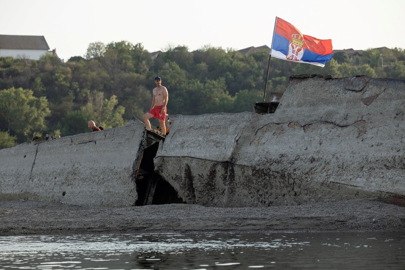 Tampilan dari drone yang memperlihatkan orang-orang berjalan di dekat bangkai kapal perang Jerman dari Perang Dunia II yang muncul ke permukaan akibat surutnya air Sungai Danube&mdash;yang disebabkan oleh kekeringan dan suhu panas ekstrem&mdash;di dekat Prahovo, Serbia, pada 13 Agustus 2026. (REUTERS/Marko Djurica)