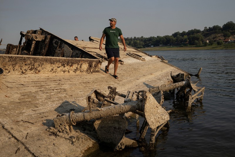 Tampilan dari drone yang memperlihatkan orang-orang berjalan di dekat bangkai kapal perang Jerman dari Perang Dunia II yang muncul ke permukaan akibat surutnya air Sungai Danube&mdash;yang disebabkan oleh kekeringan dan suhu panas ekstrem&mdash;di dekat Prahovo, Serbia, pada 13 Agustus 2026. (REUTERS/Marko Djurica)