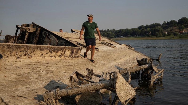 Seorang pria berdiri di atas kapal perang Jerman dari Perang Dunia II yang tenggelam dan kini muncul ke permukaan akibat surutnya air Sungai Danube—yang disebabkan oleh kekeringan dan suhu panas ekstrem—di dekat Prahovo, Serbia, pada 13 Agustus 2026.