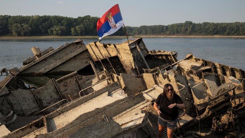 Seorang wanita berdiri di atas kapal perang Jerman dari Perang Dunia II yang tenggelam dan kini muncul ke permukaan akibat surutnya air Sungai Donau—yang disebabkan oleh kekeringan dan suhu panas ekstrem—di dekat Prahovo, Serbia, pada 13 Agustus 2026.