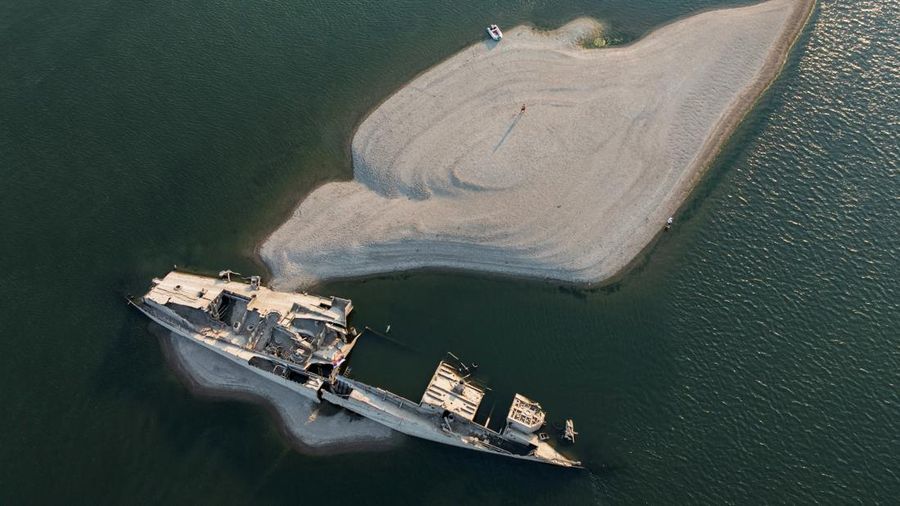 Tampilan dari drone yang memperlihatkan seorang pria berdiri di dekat bangkai kapal perang Jerman dari Perang Dunia II yang muncul ke permukaan akibat surutnya air Sungai Danube—yang disebabkan oleh kekeringan dan suhu panas ekstrem—di dekat Prahovo, Serbia, pada 13 Agustus 2026.