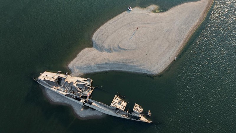 Tampilan dari drone yang memperlihatkan seorang pria berdiri di dekat bangkai kapal perang Jerman dari Perang Dunia II yang muncul ke permukaan akibat surutnya air Sungai Danube—yang disebabkan oleh kekeringan dan suhu panas ekstrem—di dekat Prahovo, Serbia, pada 13 Agustus 2026.
