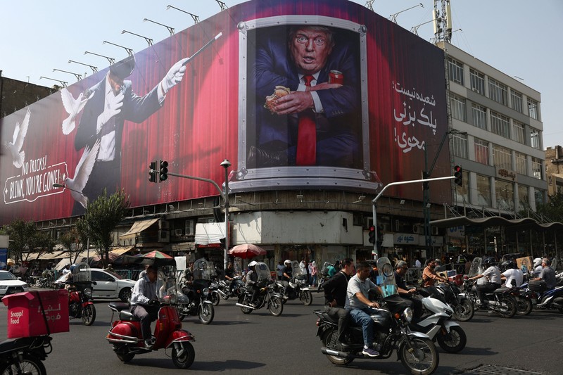 Warga berkendara di dekat papan reklame yang menampilkan Presiden AS Donald Trump pada sebuah gedung di Teheran, Iran, Senin (31/8/2026). (Majid Asgaripour/WANA via REUTERS)