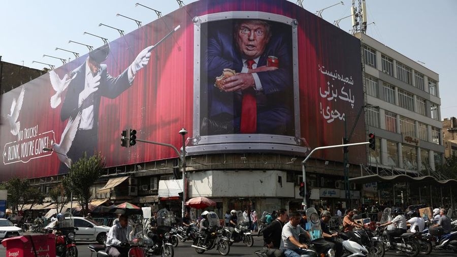 Warga berkendara di dekat papan reklame yang menampilkan Presiden AS Donald Trump pada sebuah gedung di Teheran, Iran, Senin (31/8/2026). (Majid Asgaripour/WANA via REUTERS)