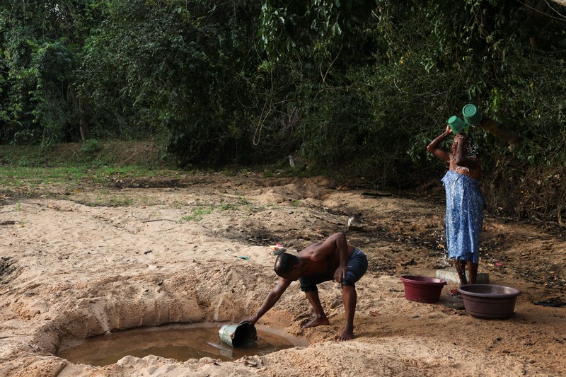 T.B. Leelawathie (49 tahun) dan temannya berjalan membawa ember dan bak saat hendak mandi di sungai yang telah mengering di Desa Galwela Yaya, Distrik Ampara, Sri Lanka, pada 27 Agustus 2026. (REUTERS/Priyanshu Singh)