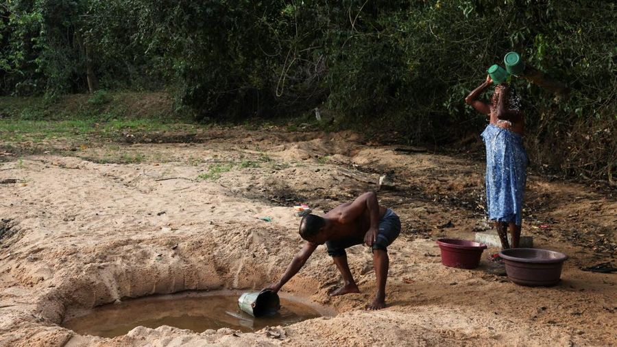 A.M. Pathmasena, 48 tahun, mengambil air dari lubang yang ia gali di dasar sungai yang mengering untuk mandi di Desa Galwela Yaya, Distrik Ampara, Sri Lanka, pada 27 Agustus 2026.