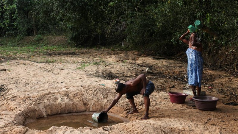 A.M. Pathmasena, 48 tahun, mengambil air dari lubang yang ia gali di dasar sungai yang mengering untuk mandi di Desa Galwela Yaya, Distrik Ampara, Sri Lanka, pada 27 Agustus 2026.