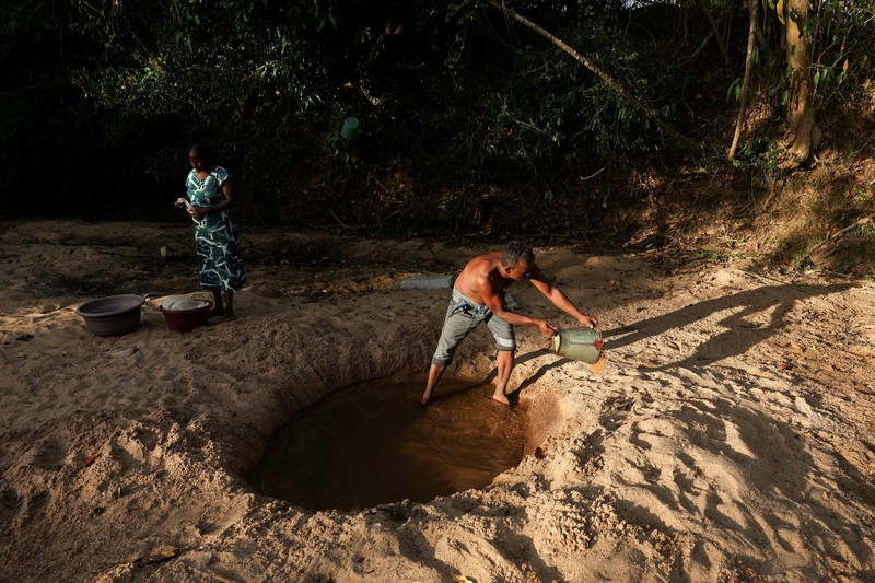 T.B. Leelawathie (49 tahun) dan temannya berjalan membawa ember dan bak saat hendak mandi di sungai yang telah mengering di Desa Galwela Yaya, Distrik Ampara, Sri Lanka, pada 27 Agustus 2026. (REUTERS/Priyanshu Singh)
