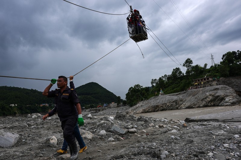 Sejumlah orang berada di dalam keranjang yang digantung pada tali luncur (zip line) darurat saat menyeberangi Sungai Trishuli dari Koloni, menyusul banjir bandang mematikan yang merusak jembatan dan sempat membuat warga terisolasi, di distrik Nuwakot, Nepal, pada 3 September 2026. (REUTERS/Athit Perawongmetha)