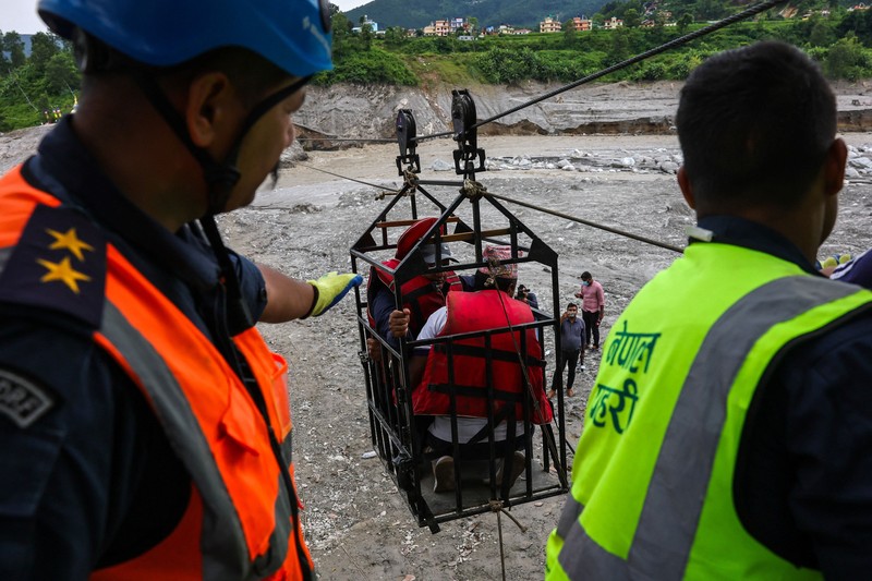 Sejumlah orang berada di dalam keranjang yang digantung pada tali luncur (zip line) darurat saat menyeberangi Sungai Trishuli dari Koloni, menyusul banjir bandang mematikan yang merusak jembatan dan sempat membuat warga terisolasi, di distrik Nuwakot, Nepal, pada 3 September 2026. (REUTERS/Athit Perawongmetha)