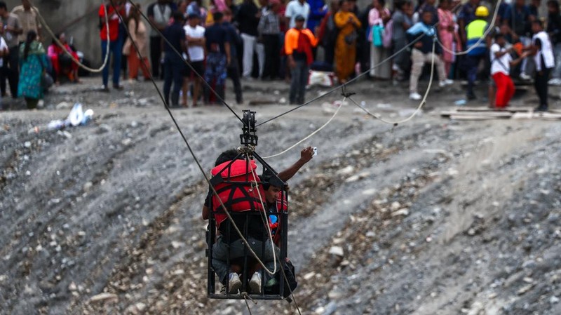 Seorang pria berswafoto saat berada di dalam keranjang gantung pada jalur *zip-line* darurat ketika menyeberangi Sungai Trishuli dari Koloni—menyusul banjir bandang mematikan yang merusak jembatan dan sempat membuat warga terisolasi—di distrik Nuwakot, Nepal, pada 3 September 2026.