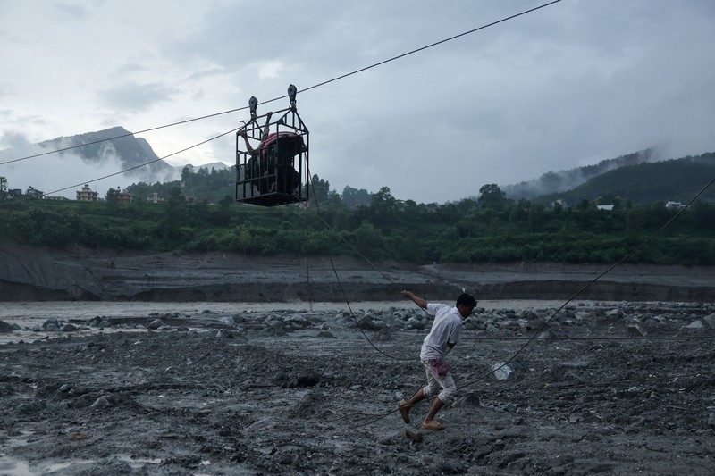 Sejumlah orang berada di dalam keranjang yang digantung pada tali luncur (zip line) darurat saat menyeberangi Sungai Trishuli dari Koloni, menyusul banjir bandang mematikan yang merusak jembatan dan sempat membuat warga terisolasi, di distrik Nuwakot, Nepal, pada 3 September 2026. (REUTERS/Athit Perawongmetha)