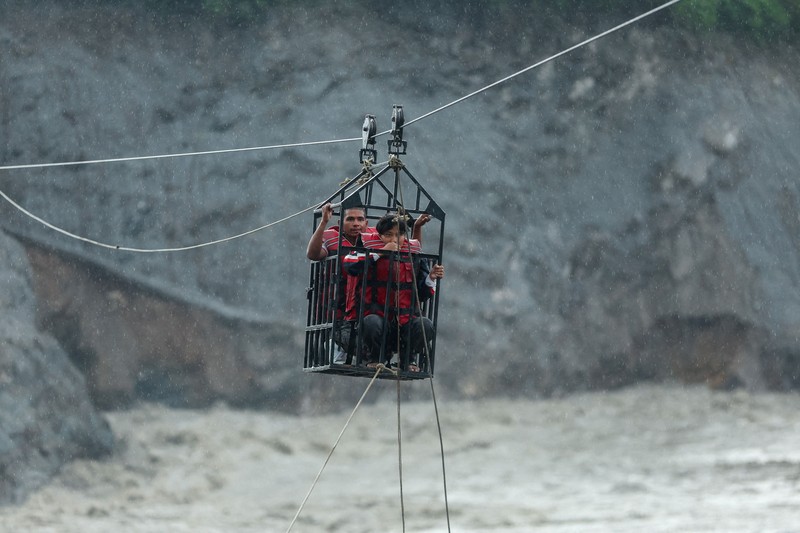 Sejumlah orang berada di dalam keranjang yang digantung pada tali luncur (zip line) darurat saat menyeberangi Sungai Trishuli dari Koloni, menyusul banjir bandang mematikan yang merusak jembatan dan sempat membuat warga terisolasi, di distrik Nuwakot, Nepal, pada 3 September 2026. (REUTERS/Athit Perawongmetha)