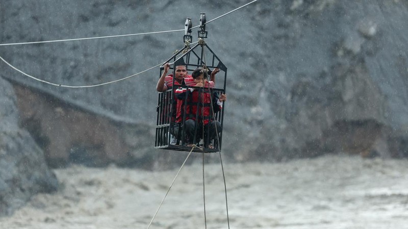 Warga berpegangan pada keranjang yang tergantung di jalur *zip-line* darurat saat menyeberangi Sungai Trishuli dari arah Koloni, setelah tanah longsor dan aliran lumpur merusak jembatan serta sempat membuat warga di Trishuli, Distrik Nuwakot, Nepal, terisolasi pada 2 September 2026.