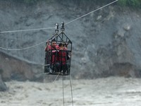 Warga berpegangan pada keranjang yang tergantung di jalur *zip-line* darurat saat menyeberangi Sungai Trishuli dari arah Koloni, setelah tanah longsor dan aliran lumpur merusak jembatan serta sempat membuat warga di Trishuli, Distrik Nuwakot, Nepal,
