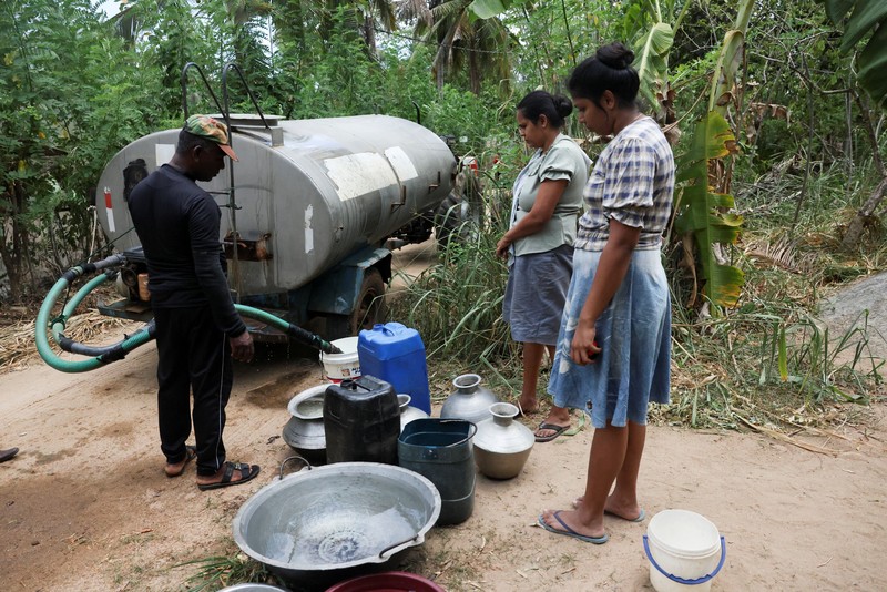 T.B. Leelawathie (49 tahun) dan temannya berjalan membawa ember dan bak saat hendak mandi di sungai yang telah mengering di Desa Galwela Yaya, Distrik Ampara, Sri Lanka, pada 27 Agustus 2026. (REUTERS/Priyanshu Singh)